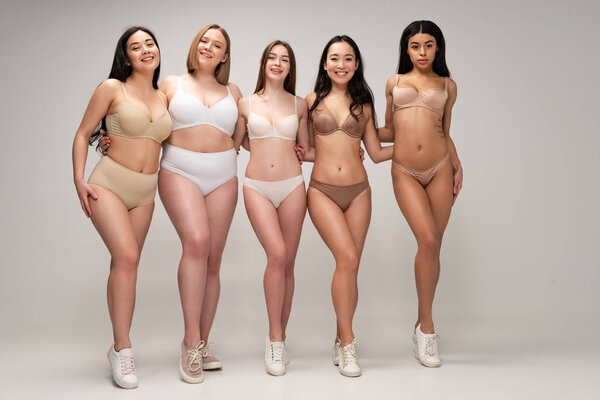 five cheerful multiethnic girls in underwear hugging while looking at camera, body positivity concept