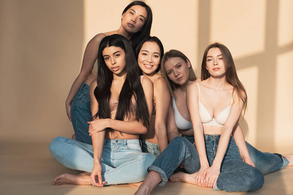 пять привлекательных мультикультурных девушек в синих джинсах и бюстгальтерах, улыбающихся, глядя в камеру
