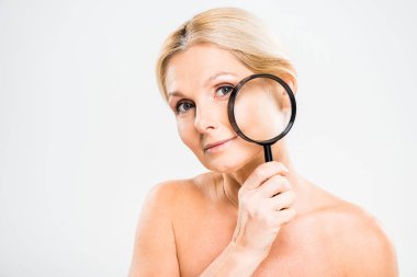 beautiful and blonde mature woman holding loupe and looking at camera on grey background  clipart