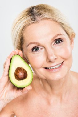 Avokado tutarak ve gri izole kamera bakıyor güzel ve gülümseyen kadın