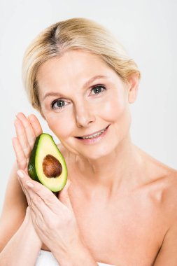 Avokado tutarak ve gri izole kamera seyir çekici ve gülümseyen kadın