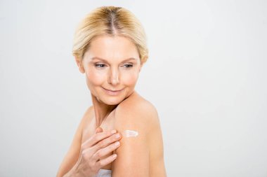 beautiful and mature woman looking down and applying cosmetic cream on shoulder 