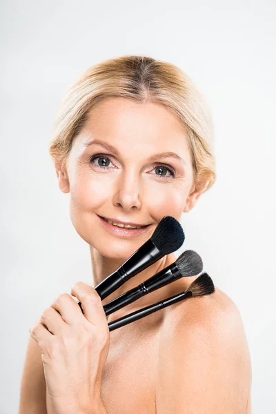 Hermosa Sonriente Mujer Madura Mirando Cámara Celebración Cepillos Cosméticos Sobre — Foto de Stock