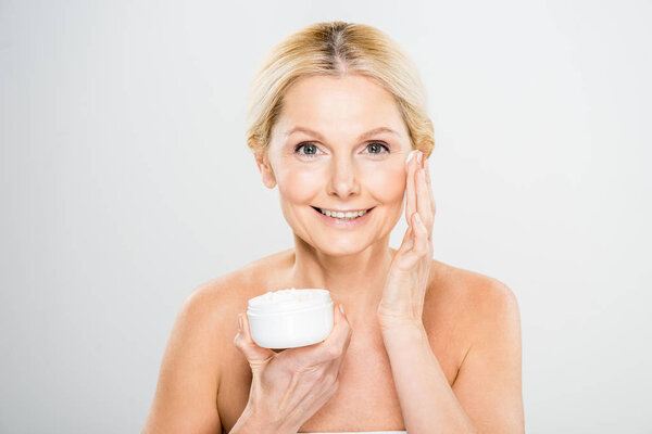 beautiful and smiling woman looking at camera and applying cosmetic cream