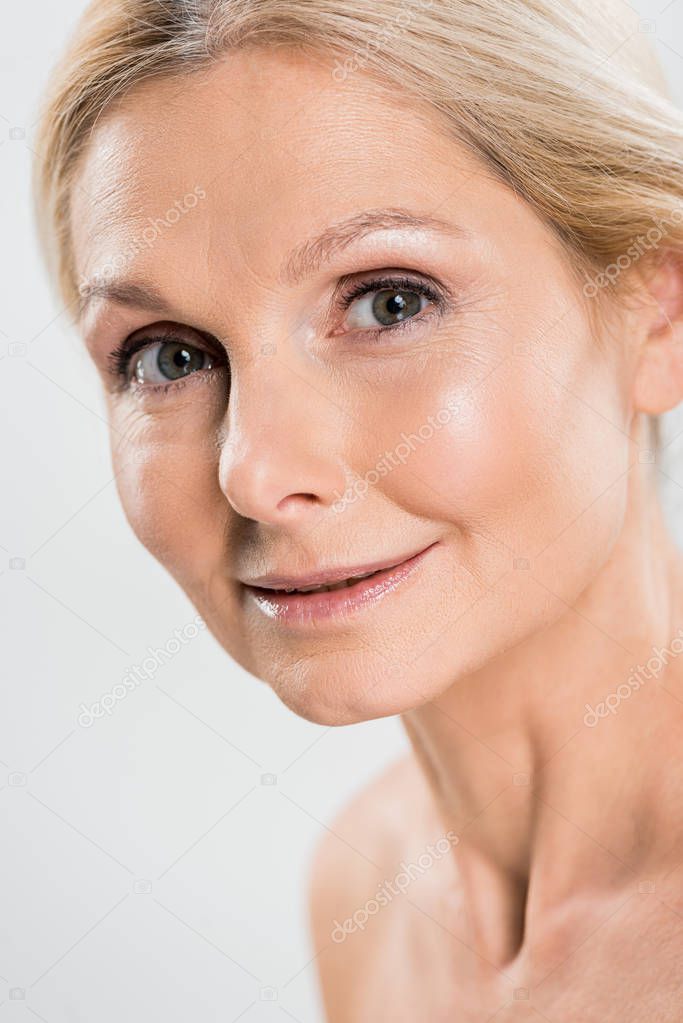 close up of beautiful and blonde mature woman looking at camera isolated on grey 