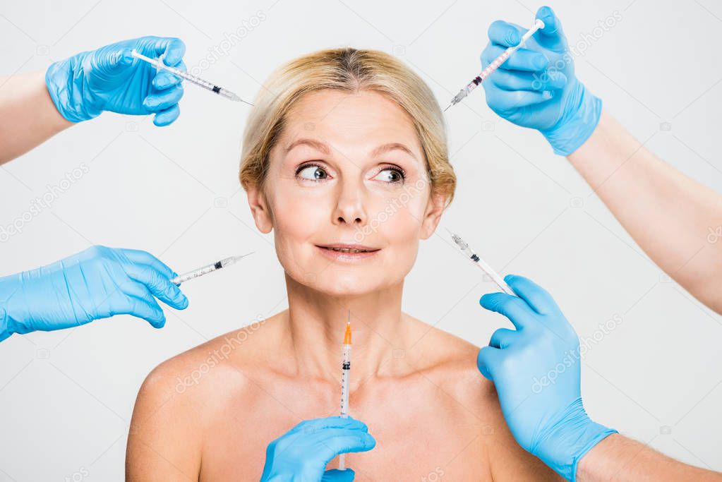 beautiful and mature woman looking away with cosmetologists holding syringes