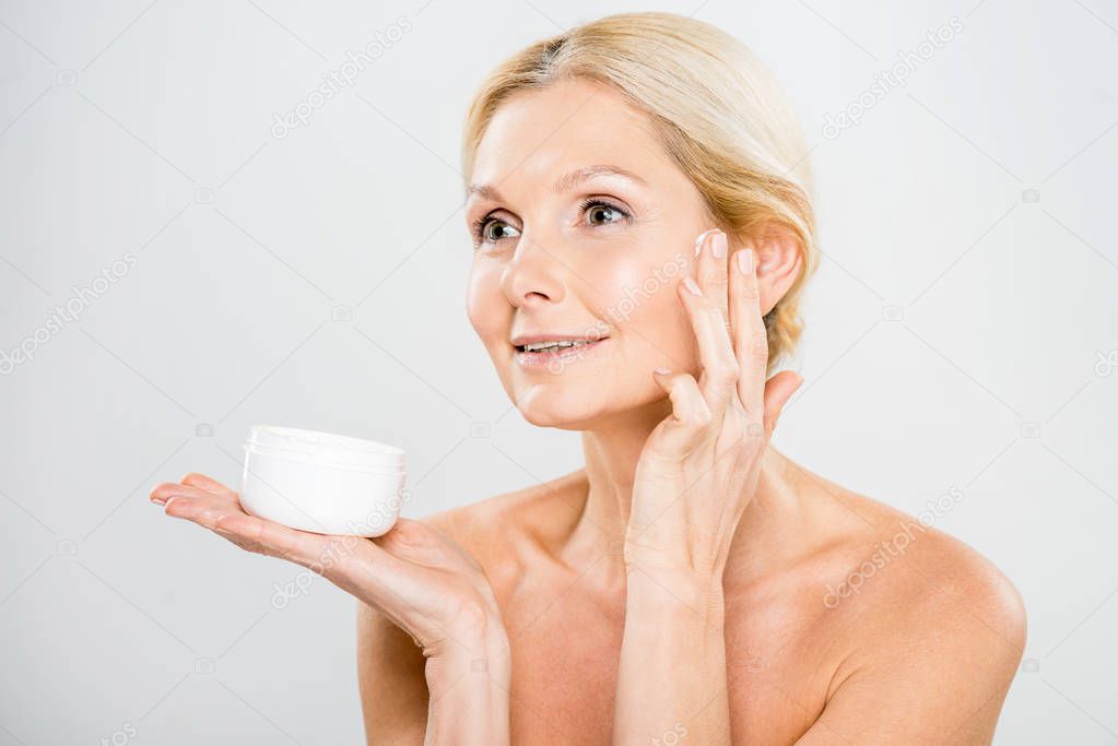 beautiful and smiling woman looking away and applying cosmetic cream