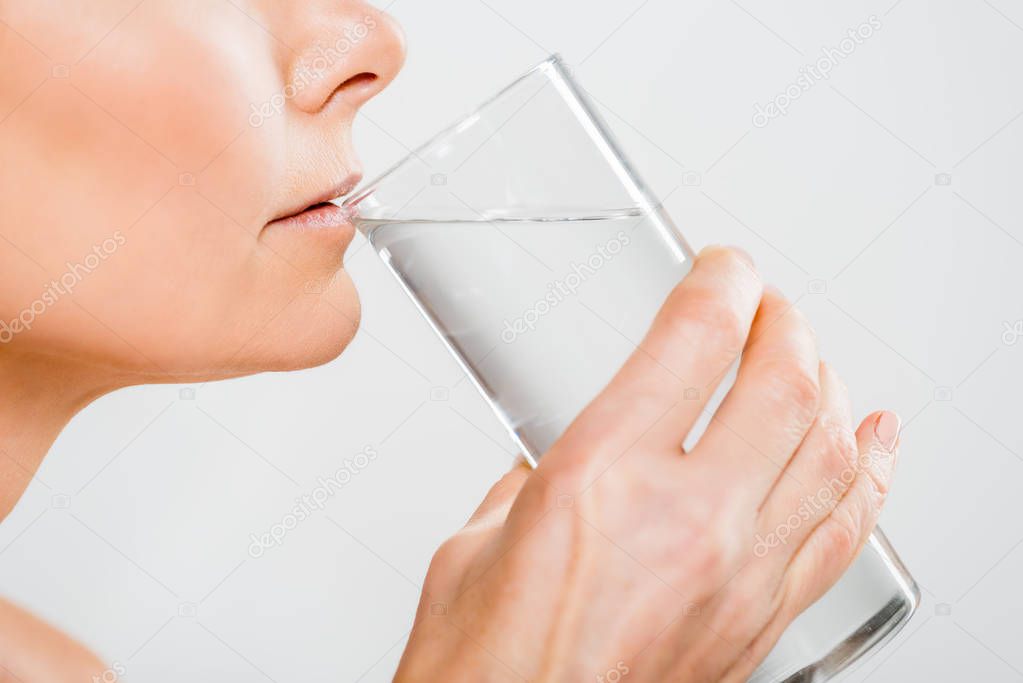 cropped view of mature woman drinking water from glass isolated on grey 