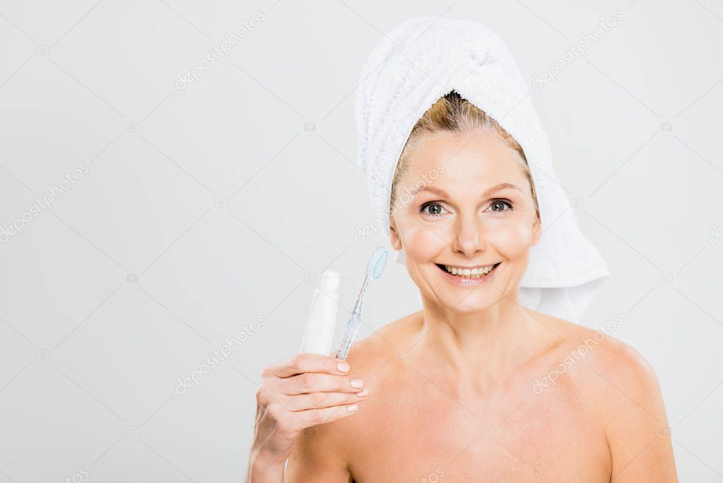 beautiful and smiling mature woman in towel holding toothpaste and toothbrush