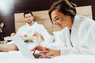 seçici odak neşeli kadın erkek yatakta yatarken yakınındaki dizüstü bilgisayar kullanarak 