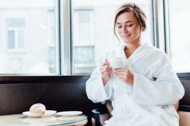 gülümseyen ve kahve Kupası'nda seyir bornoz çekici esmer kadın