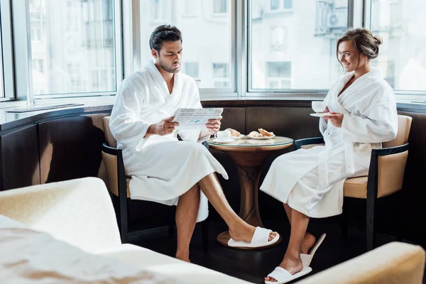 Fröhliche Frau Schaut Gutaussehenden Mann Beim Zeitungslesen Bademantel — Stockfoto