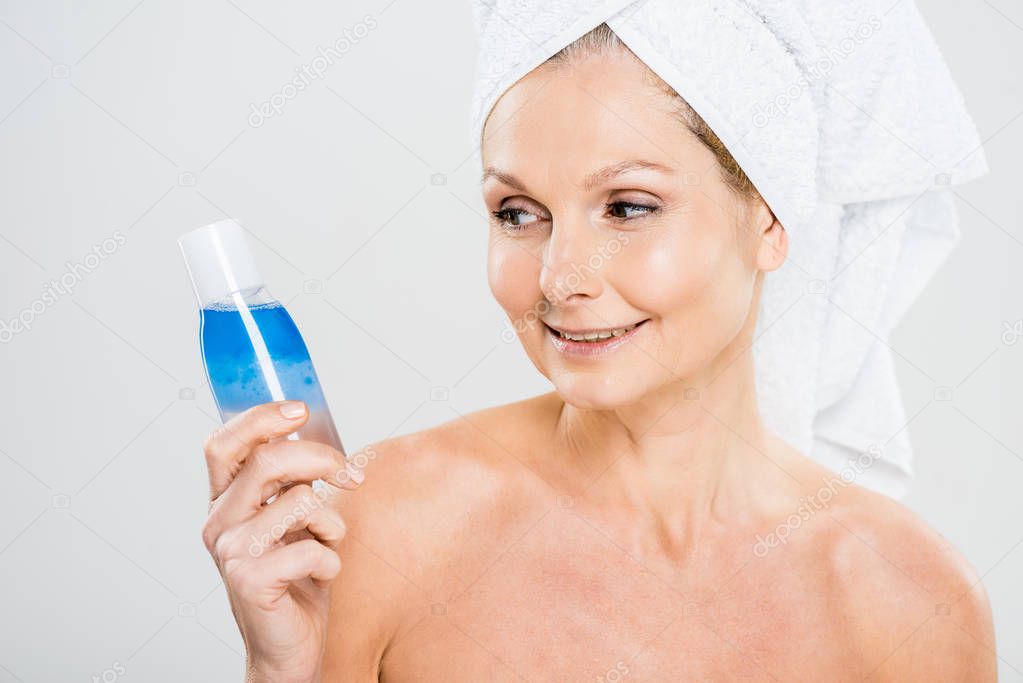 attractive and smiling mature woman in towel holding bottle with micellar water 