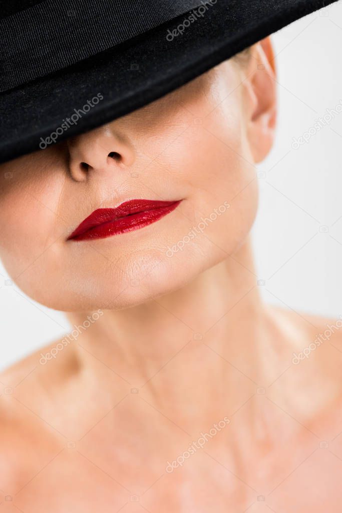 selective focus of middle aged elegant and fashionable woman with red lips in black hat isolated on grey 