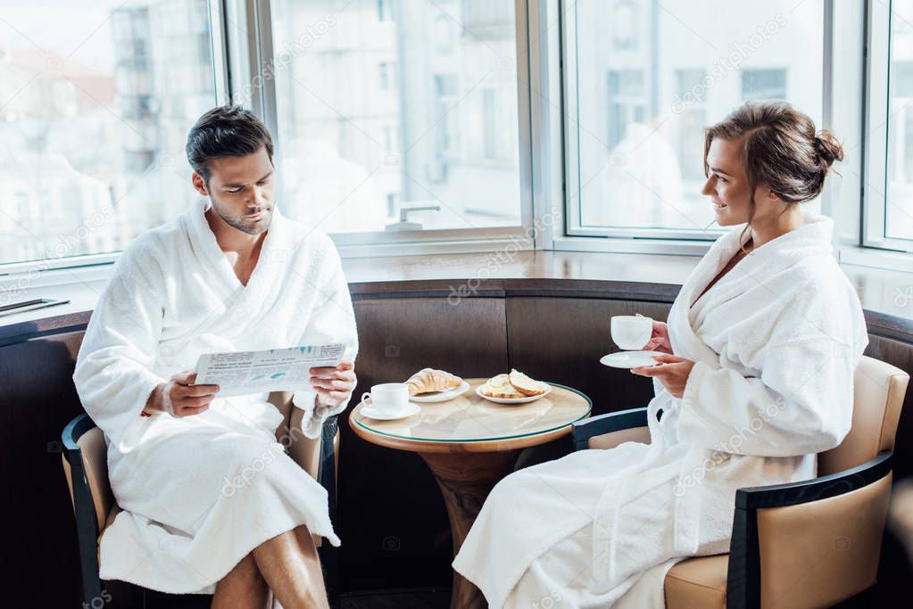 attractive woman looking at handsome man reading newspaper in bathrobe 