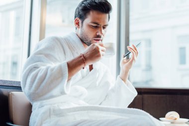 yakışıklı adam beyaz bornoz smartphone ve fincan kahve ile tutarak sakallı