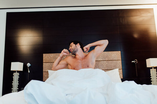 handsome muscular man stretching in bed after wake up in hotel