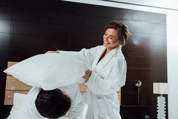 Feliz Pareja Albornoces Teniendo Pelea Almohadas Cama Hotel —  Fotos de Stock