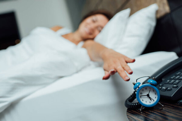 selective focus of retro blue alarm clock near woman in bed