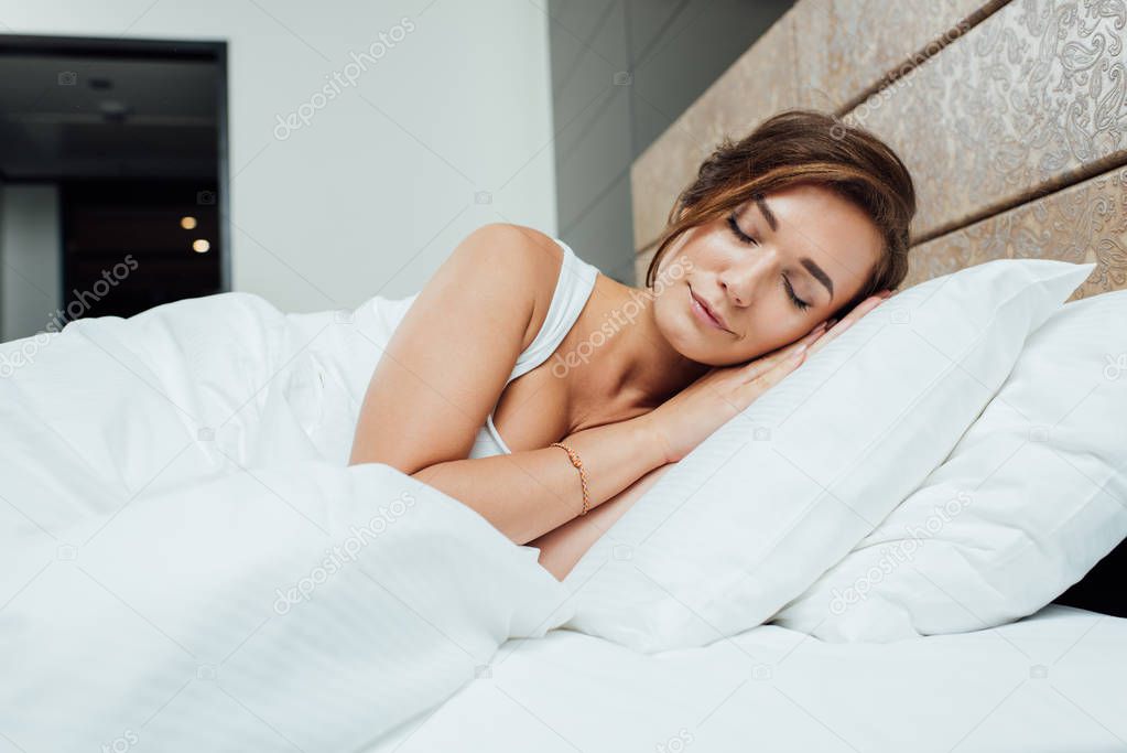 attractive brunette woman sleeping on pillows under blanket in bed 