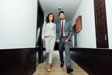 neşeli işadamı ve mutlu işkadını elele ve otel koridorda yürürken formal giyim 