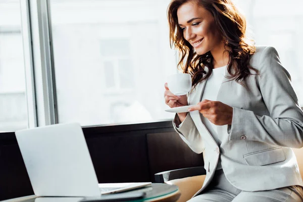 Alegre Mujer Negocios Usando Ordenador Portátil Mientras Sostiene Taza Café —  Fotos de Stock