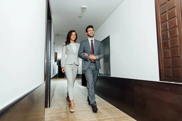 cheerful businessman and businesswoman in formal wear walking hotel corridor