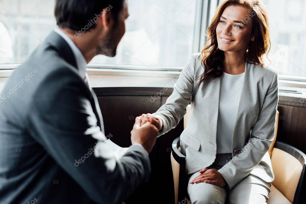 selective focus of happy businesswoman shaking hands with businessman 