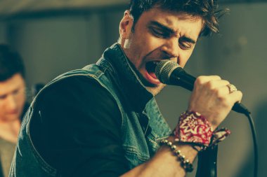 selective focus of handsome stylish man singing in microphone  clipart