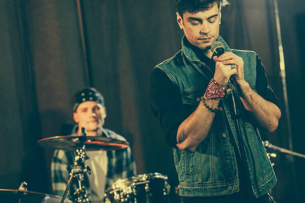 handsome man standing near microphone with closed eyes near drummer 