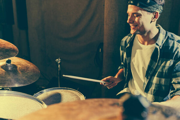 selective focus of cheerful drummer holding drum sticks while playing drums 