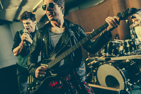 selective focus of cheerful guitarist in sunglasses playing electric guitar near rock band 