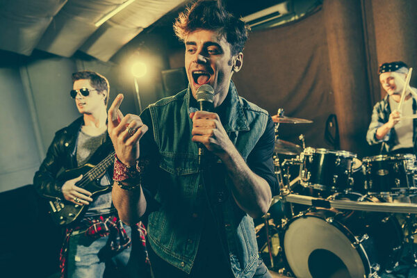 selective focus of stylish singer singing in microphone near guitarist in sunglasses and drummer 