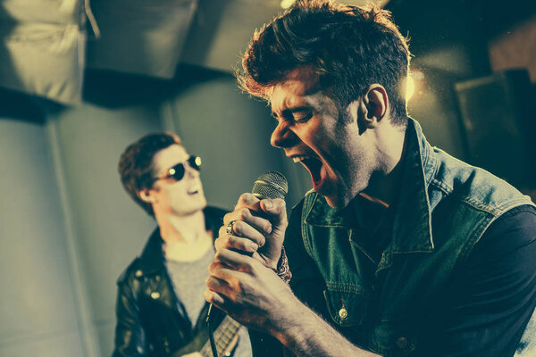 selective focus of stylish singer singing in microphone near rock band