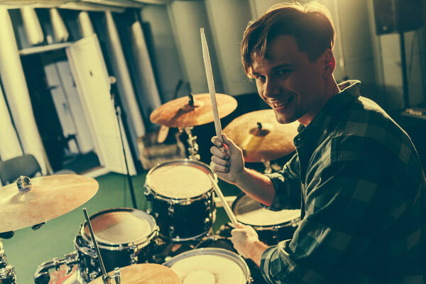 happy good-looking musician holding drum sticks near drums