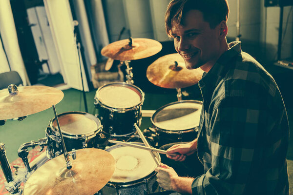 cheerful good-looking musician holding drum sticks near drums