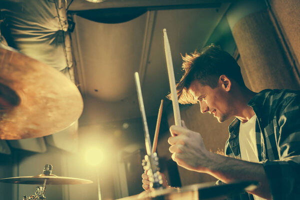 cheerful good-looking drummer holding drum sticks while playing drums