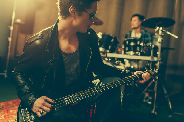 stylish guitarist in sunglasses playing electric guitar near drummer 