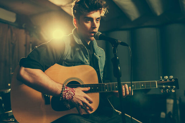 good-looking musician singing in microphone while playing acoustic guitar 