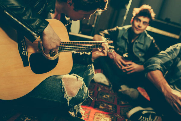selective focus of musician playing acoustic guitar near friends 