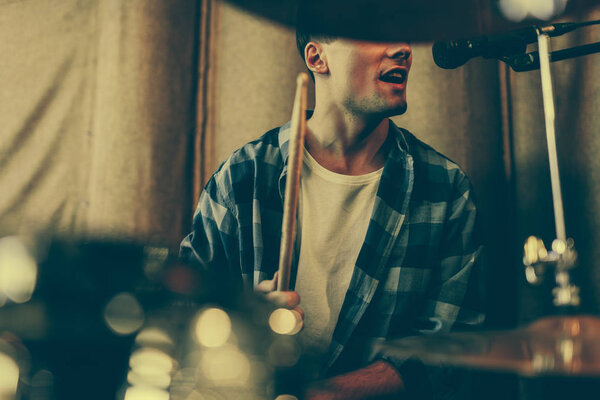 cropped view of man singing in microphone while playing drums 