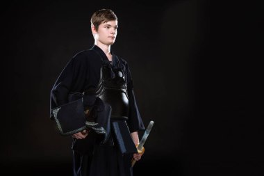 Young man holding kendo helmet and bamboo sword on black clipart