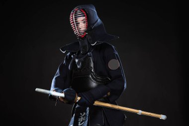 Kendo fighter in helmet holding bamboo sword and looking away on black clipart
