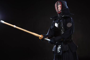 Kendo fighter in traditional helmet holding bamboo sword on black clipart