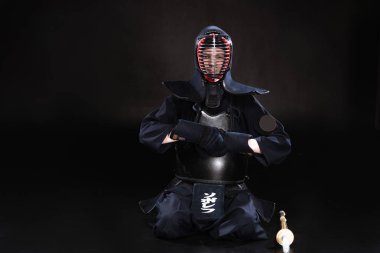 Kendo fighter in helmet sitting on floor and taking off gloves on black clipart