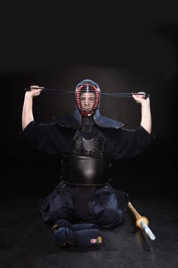 Kendo fighter in armor tying helmet on black clipart