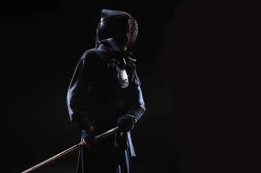 Kendo fighter in helmet holding bamboo sword on black clipart