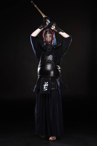 Полный обзор бойца кэндо в доспехах, практикующегося с бамбуковым мечом на черном
