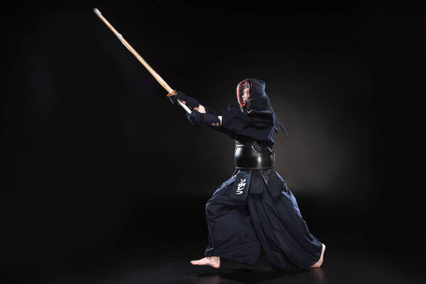 Полный обзор бойца кэндо в доспехах, практикующегося с бамбуковым мечом на черном
