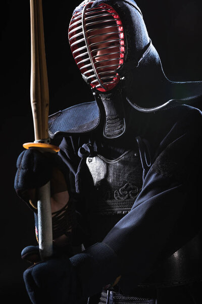 Боец Кендо в шлеме держит бамбуковый меч изолированный на черном
